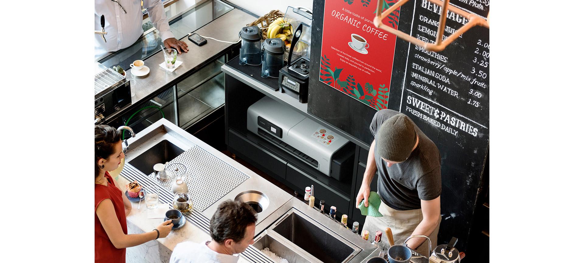 Homme travaillant derrière le comptoir d’un petit restaurant. L’imprimante grand format Canon imagePROGRAF TC-21 est posée sur une étagère derrière lui.