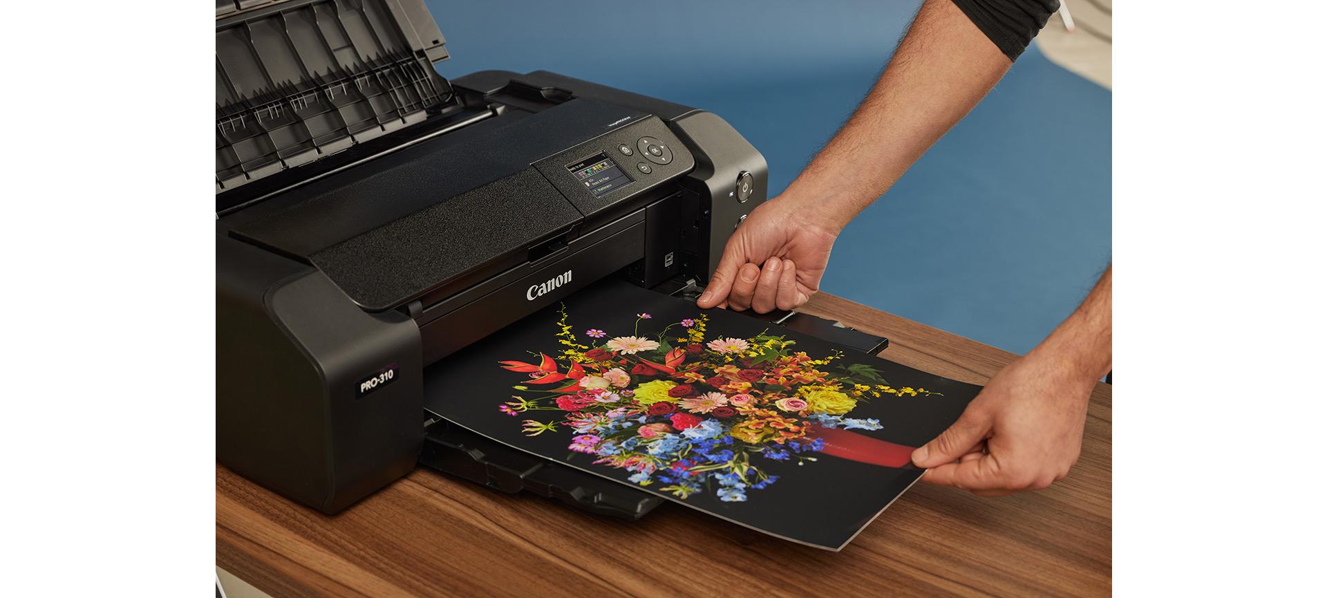 A man using a Canon PIXMA PRO-310 to print a photo of a vase of flowers.