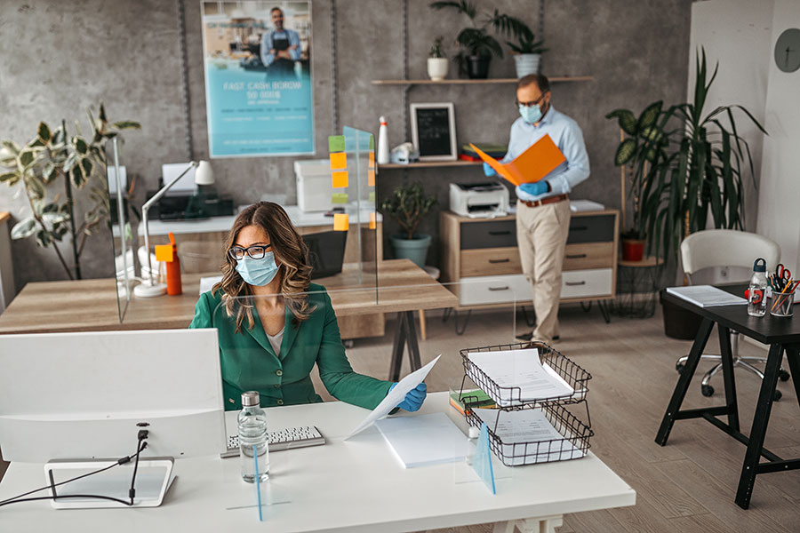 Man and woman, both masked, working in office environment
